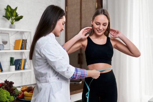 A nutritionist in his office measures the volume of his patient's waist. The doctor advises the young beautiful girl how to follow a diet and be healthy.